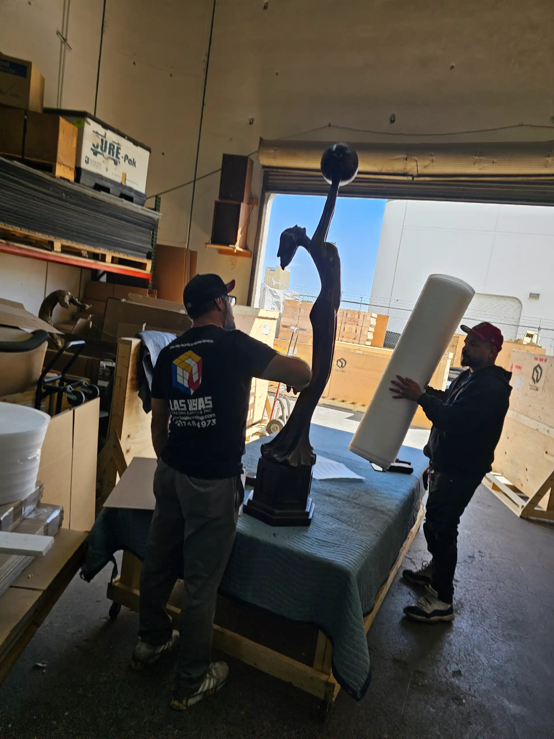 Staff carefully handling a tall bronze sculpture in the warehouse